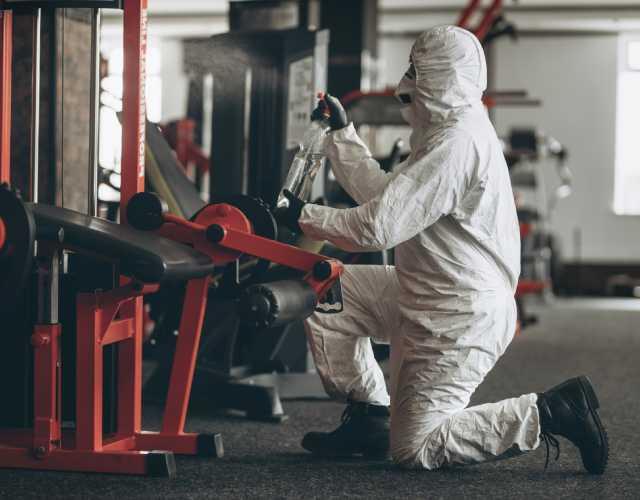 Worker sanitizing gym equipment